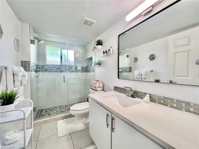 Bathroom featuring a shower with shower door, tile floors, tasteful backsplash, vanity, and toilet