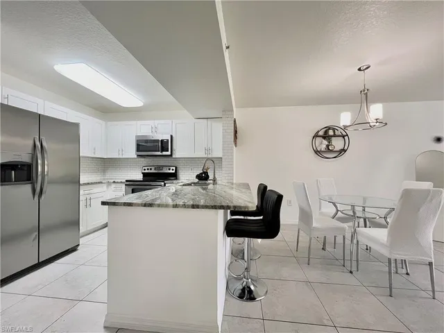 Kitchen featuring kitchen peninsula, stainless steel appliances, dark stone countertops, backsplash, and light tile floors