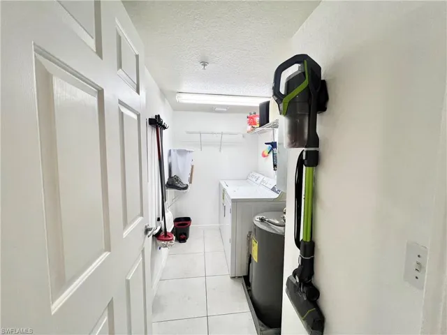 Washroom with light tile flooring, a textured ceiling, and washing machine and dryer