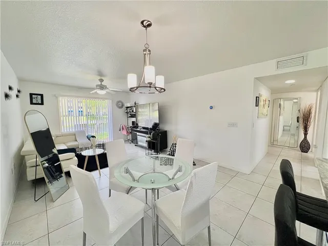 Tiled dining room with a textured ceiling and ceiling fan with notable chandelier