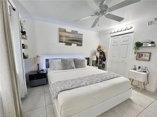 Bedroom with ceiling fan, a closet, a textured ceiling, and light tile floors
