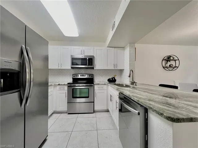 Kitchen featuring backsplash, appliances with stainless steel finishes, and white cabinets