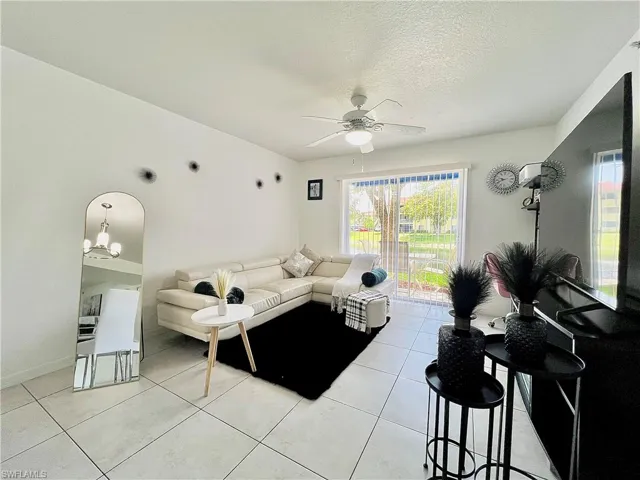 Living room featuring ceiling fan with notable chandelier and light tile floors