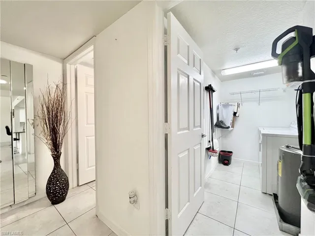 Hall with washing machine and dryer, a textured ceiling, and light tile floors