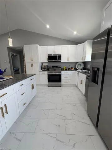 Kitchen featuring white cabinetry with gold-finish hardware, stainless steel appliances, and dark speckled countertops