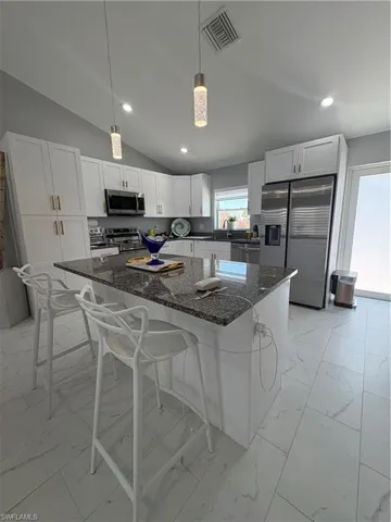 Kitchen featuring a central island with a granite countertop, white cabinetry, stainless steel appliances, and tile flooring