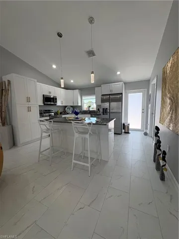 Spacious kitchen featuring white cabinetry, a large island with a stone-finish countertop, stainless steel appliances, and sleek tile flooring