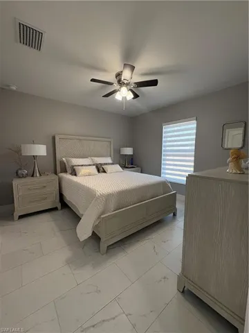 Spacious bedroom featuring light-toned tile flooring, a ceiling fan with integrated lighting, and a window with horizontal blinds