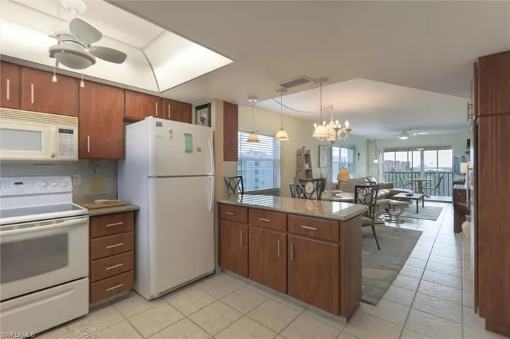 Kitchen with pendant lighting, white appliances, light tile floors, and ceiling fan with notable chandelier
