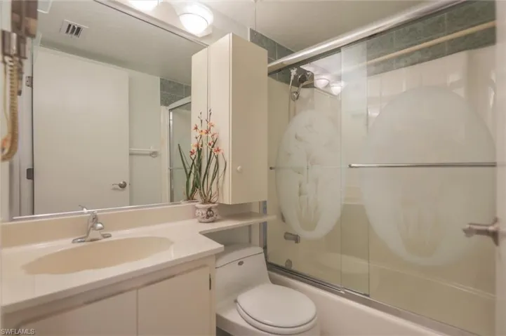 Full bathroom with enclosed tub / shower combo, vanity, and toilet