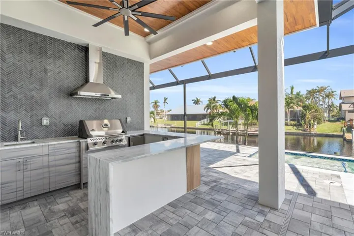 Kitchen with a water view, wall chimney range hood, ceiling fan, wooden ceiling, and sink