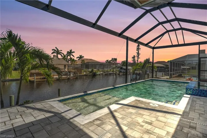 Pool at dusk featuring a lanai, a water view, and a patio