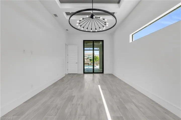Spare room featuring a notable chandelier, light wood-type flooring, and a high ceiling