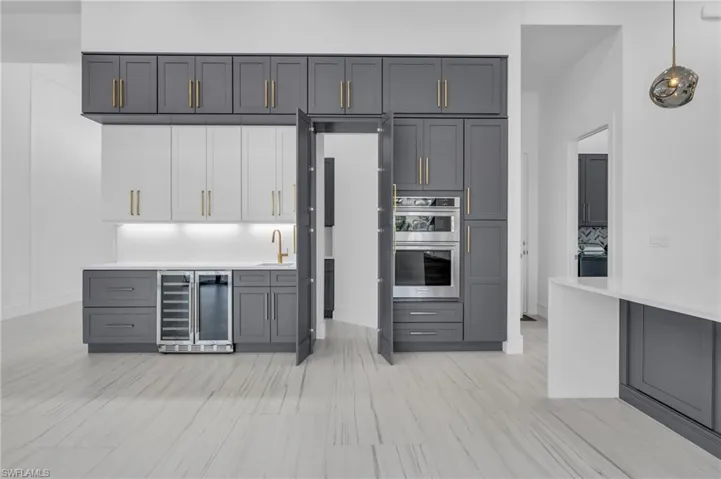 Kitchen with gray cabinetry, wine cooler, sink, hanging light fixtures, and double oven