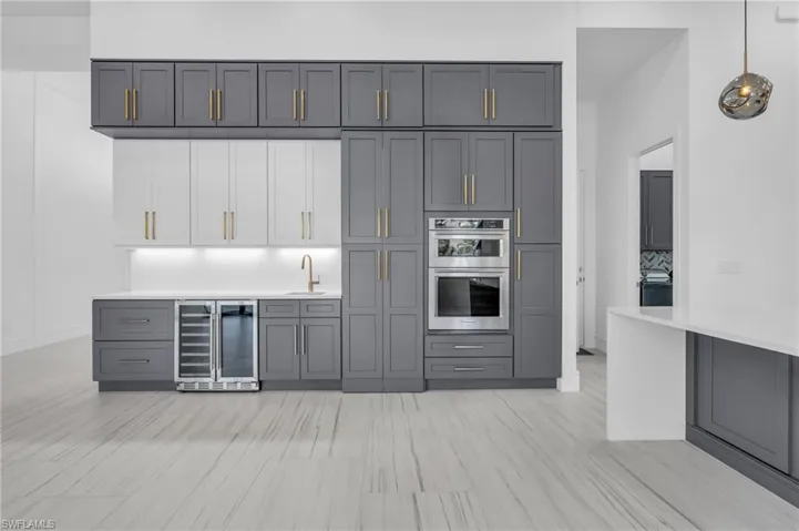 Kitchen with double oven, gray cabinetry, beverage cooler, sink, and decorative light fixtures
