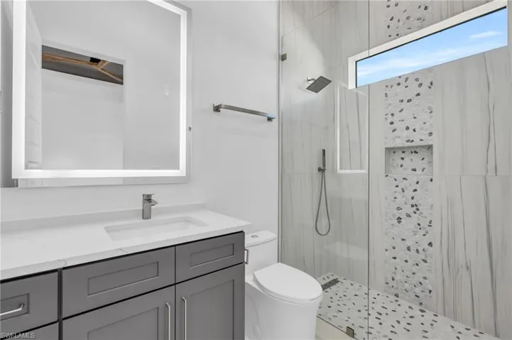 Bathroom featuring a tile shower, vanity, and toilet