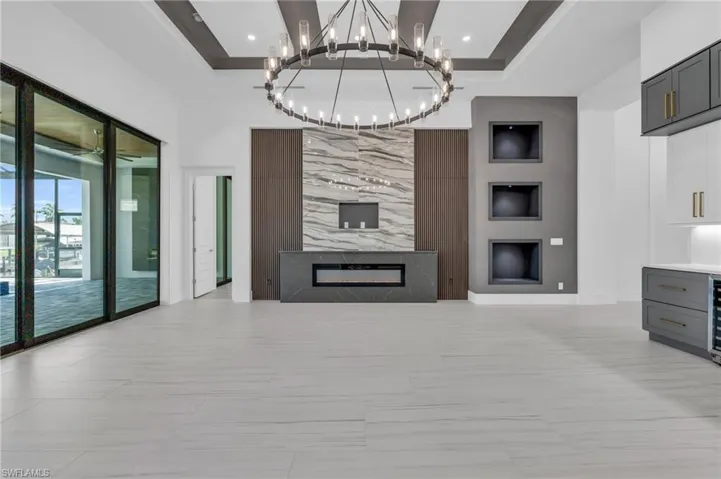 Living room featuring a raised ceiling, a premium fireplace, beverage cooler, and a notable chandelier