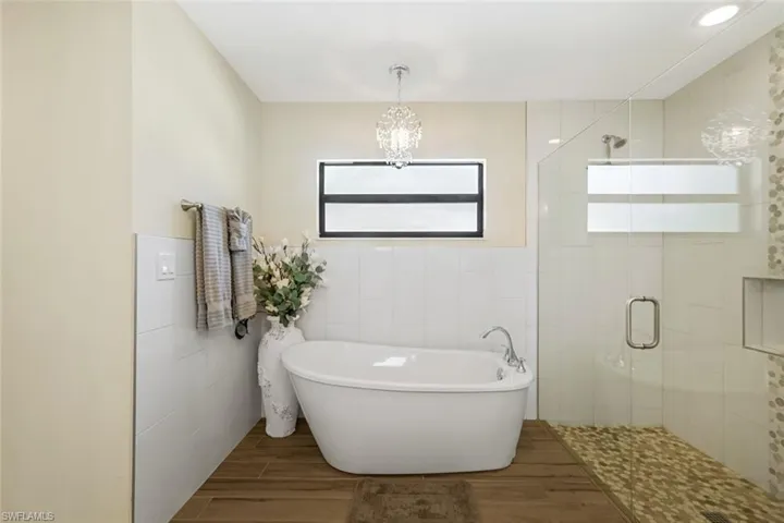 Bathroom featuring plus walk in shower, wood-type flooring, a chandelier, and tile walls