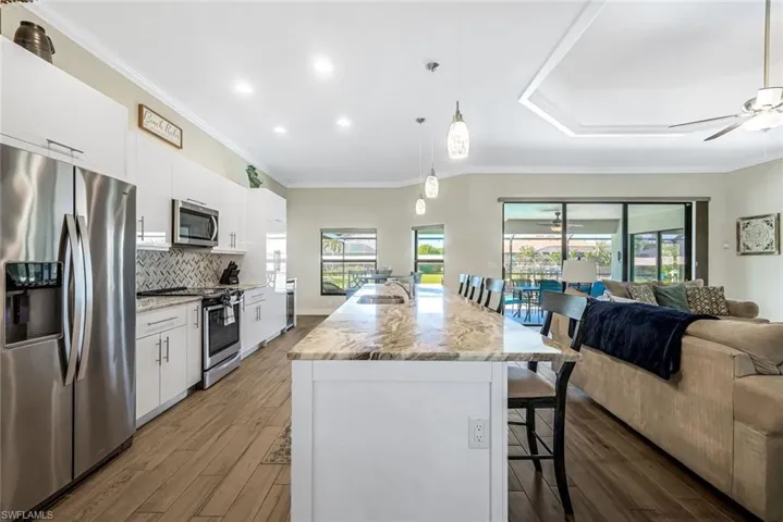 Kitchen with a wealth of natural light, stainless steel appliances, a kitchen island with sink, white cabinets, and dark hardwood / wood-style floors