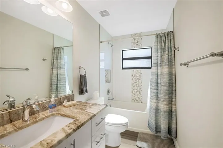 Full bathroom featuring shower / bath combo with shower curtain, vanity, wood-type flooring, and toilet