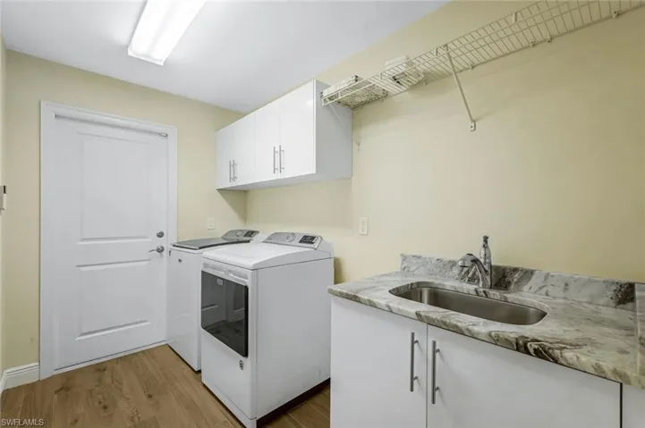 Laundry room featuring cabinets, washing machine and dryer, light wood-type flooring, and sink