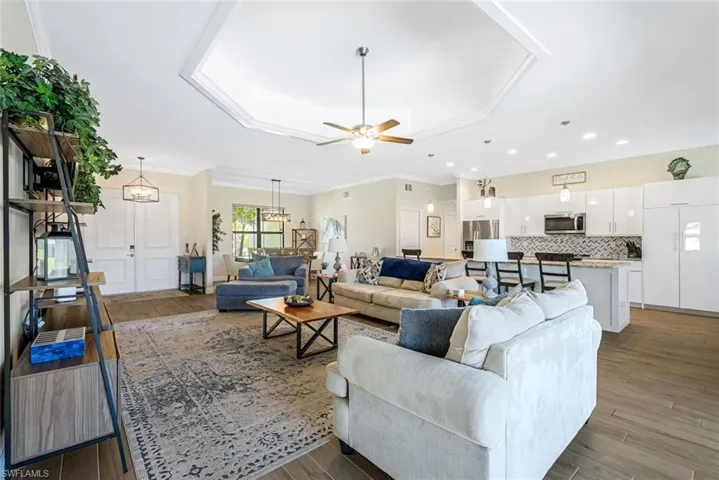 Living room featuring hardwood / wood-style floors, ceiling fan with notable chandelier, a raised ceiling, and crown molding