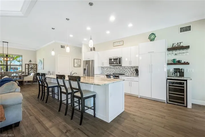 Kitchen with appliances with stainless steel finishes, beverage cooler, white cabinets, hanging light fixtures, and an island with sink