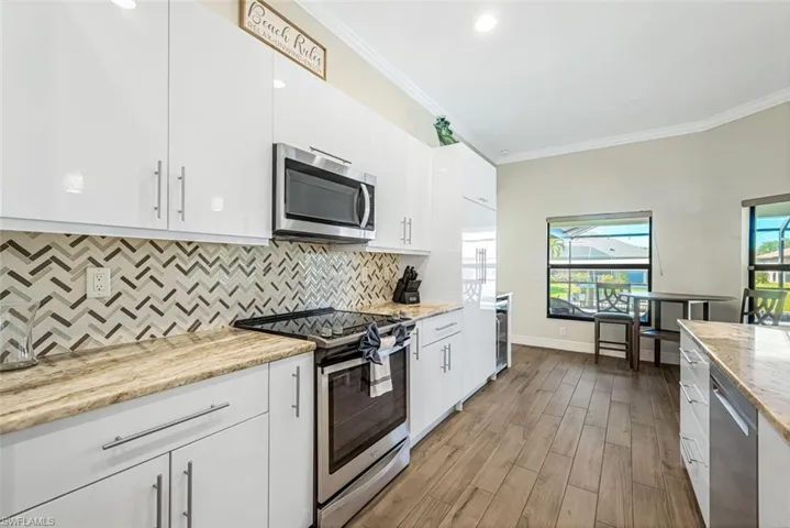 Kitchen with light stone countertops, white cabinetry, stainless steel appliances, and ornamental molding