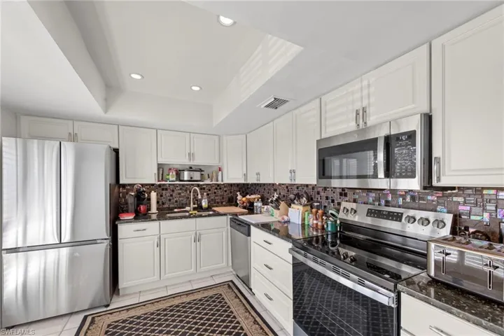 Kitchen featuring stainless steel appliances, white cabinetry, recessed lighting, dark stone countertops, and a tray ceiling