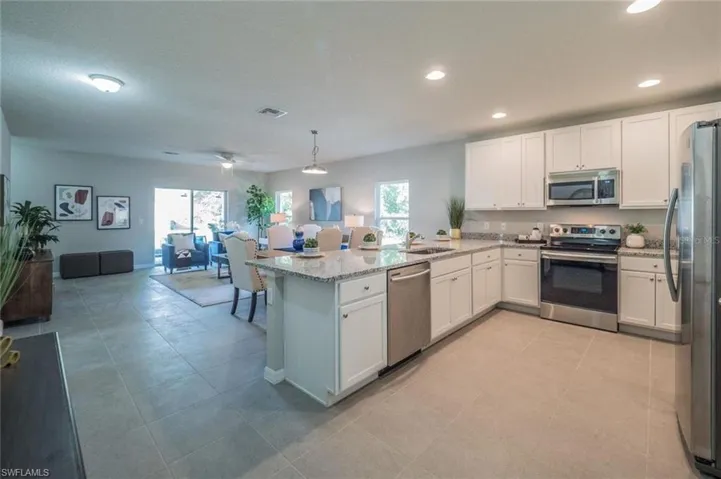 Kitchen with stainless steel appliances, open floor plan, white cabinetry, light stone counters, and a peninsula