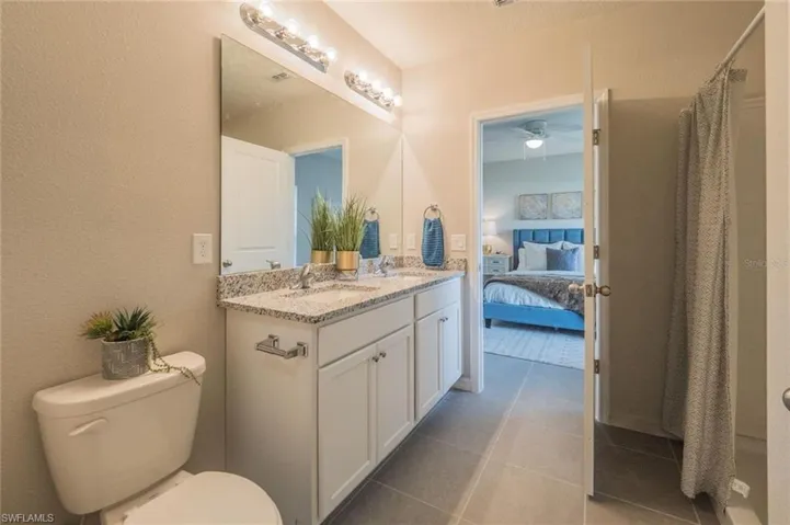 Full bath with a shower with shower curtain, double vanity, connected bathroom, a textured wall, and light tile patterned flooring