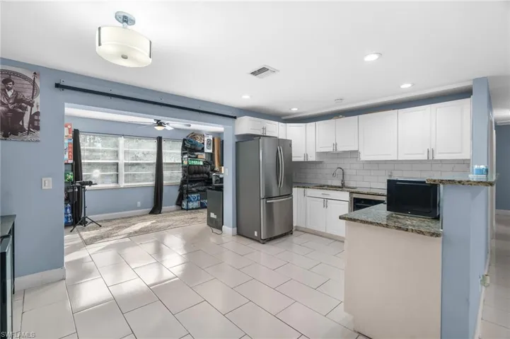 Kitchen with dark stone countertops, white cabinetry, freestanding refrigerator, ceiling fan, and tasteful backsplash