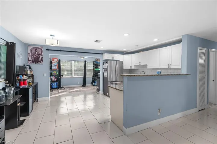 Kitchen featuring dark stone countertops, white cabinetry, freestanding refrigerator, a peninsula, and backsplash