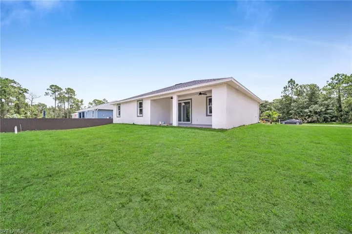 Back of house featuring a lawn, fence, ceiling fan, and stucco siding