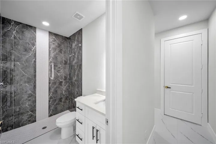 Bathroom with a tile shower, marble finish floor, visible vents, and vanity