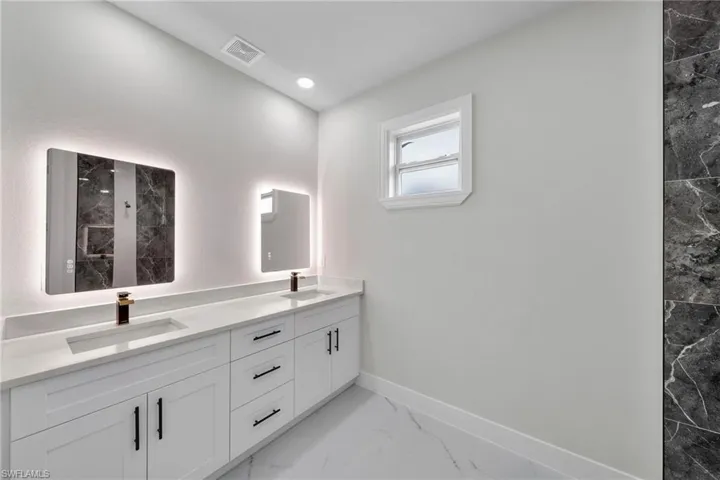 Bathroom featuring baseboards, marble finish floor, double vanity, and a sink