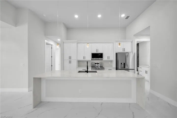 Kitchen featuring appliances with stainless steel finishes, a large island, a sink, white cabinetry, and visible vents