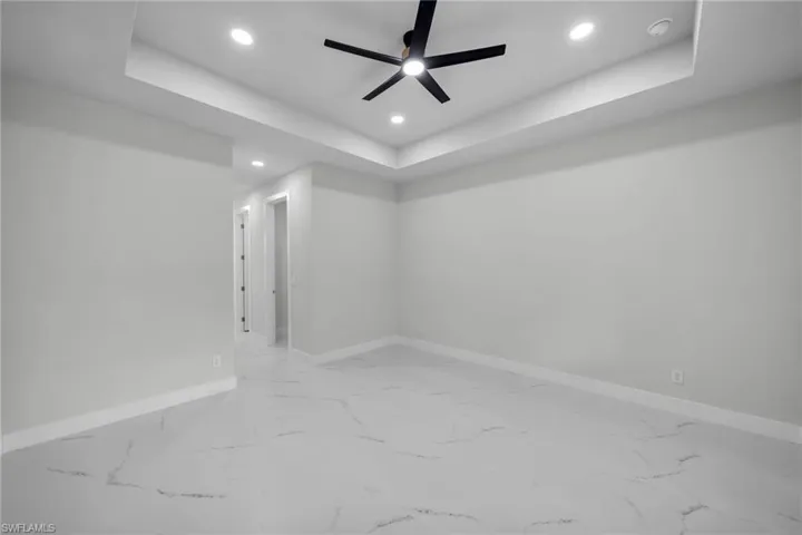 Empty room with baseboards, recessed lighting, a raised ceiling, and marble finish floor
