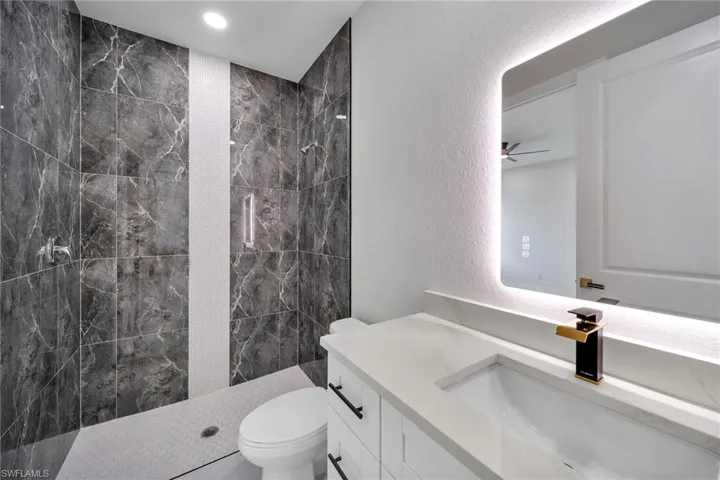 Full bath with walk in shower, toilet, a textured wall, vanity, and a ceiling fan