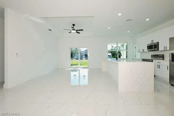 Kitchen with white cabinets, appliances with stainless steel finishes, a center island with sink, light marble finish floors, and recessed lighting