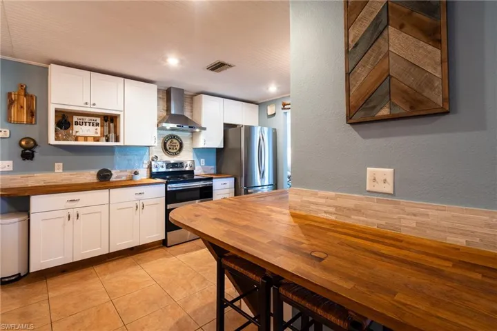 Kitchen with wood counters, tasteful backsplash, wall chimney range hood, stainless steel appliances, and white cabinets