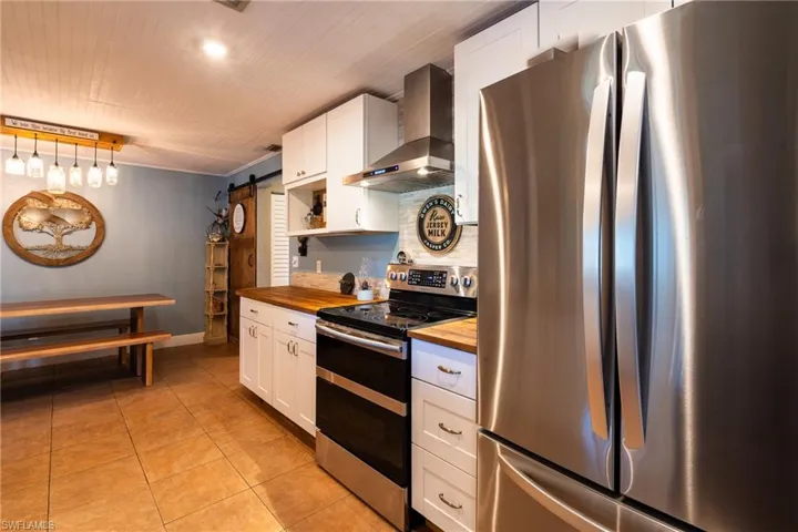 Kitchen with white cabinets, wooden counters, exhaust hood, stainless steel appliances, and a barn door