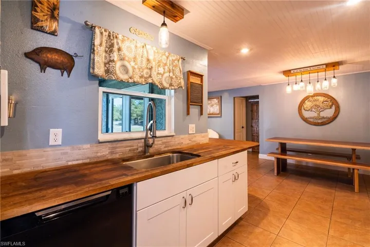 Kitchen featuring sink, butcher block countertops, white cabinetry, decorative light fixtures, and black dishwasher