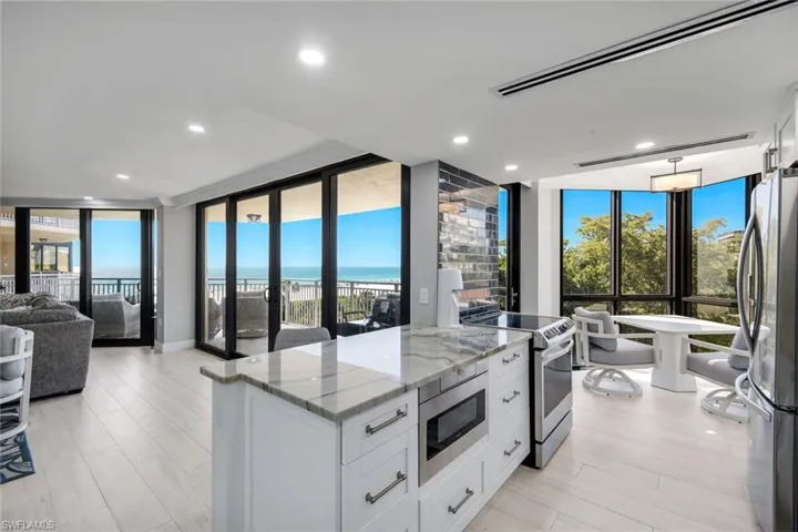 Open concept living area featuring light-toned flooring, a kitchen island with a stone countertop, and stainless steel appliances