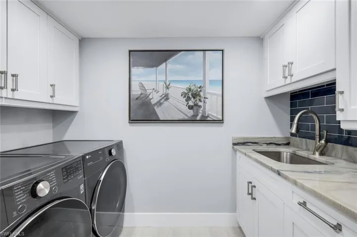 The laundry area features white cabinetry with brushed nickel hardware, a utility sink set into a light-colored countertop, and a dark blue subway tile backsplash