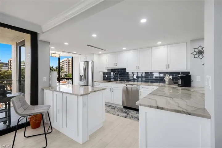 Contemporary kitchen featuring white cabinetry, stone countertops, stainless steel appliances, and a dark tile backsplash