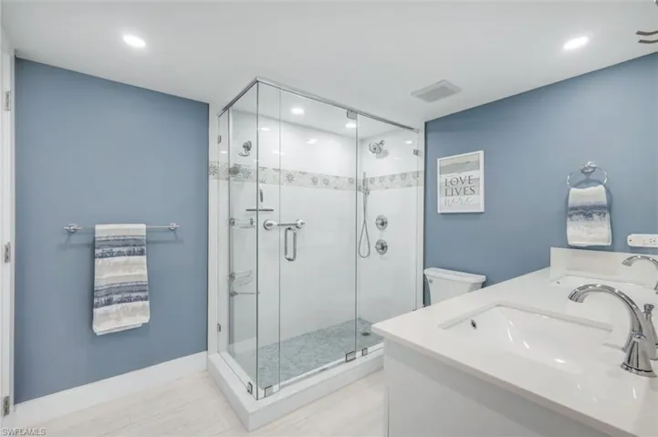 The bathroom features a spacious glass-enclosed shower with tile work, a dual vanity with undermount sinks, and contemporary fixtures