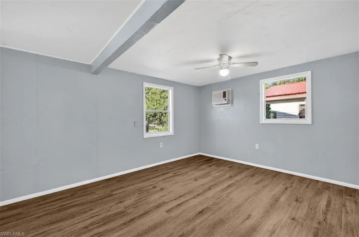 Unfurnished room with beam ceiling, wood finished floors, healthy amount of natural light, and a ceiling fan