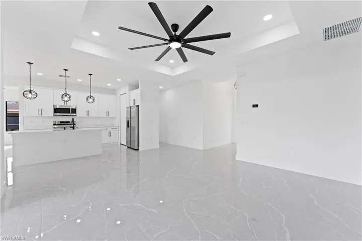 Unfurnished living room with ceiling fan, sink, and a tray ceiling