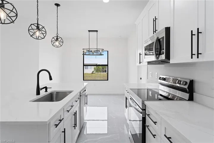 Kitchen featuring white cabinets, sink, light stone countertops, decorative light fixtures, and stainless steel appliances